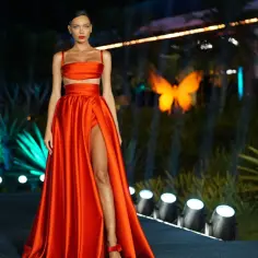 Modelka w ognistoczerwonej sukni z rozcięciem prezentuje kreację na tle nocnego ogrodu hotelu Paradise 11.