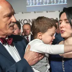 Janusz Korwin-Mikke z dziećmi na rękach, w tle konferencja.