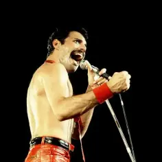 Freddie Mercury w czerwonych spodniach i opasce na nadgarstku śpiewa do mikrofonu. Nawet jako dorosły, jego energia przypominała dzikie dziecięce zabawy.