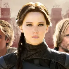 Igrzyska Śmierci obsada: Jennifer Lawrence jako Katniss, Liam Hemsworth jako Gale i Woody Harrelson jako Haymitch na tle dystopijnego miasta.