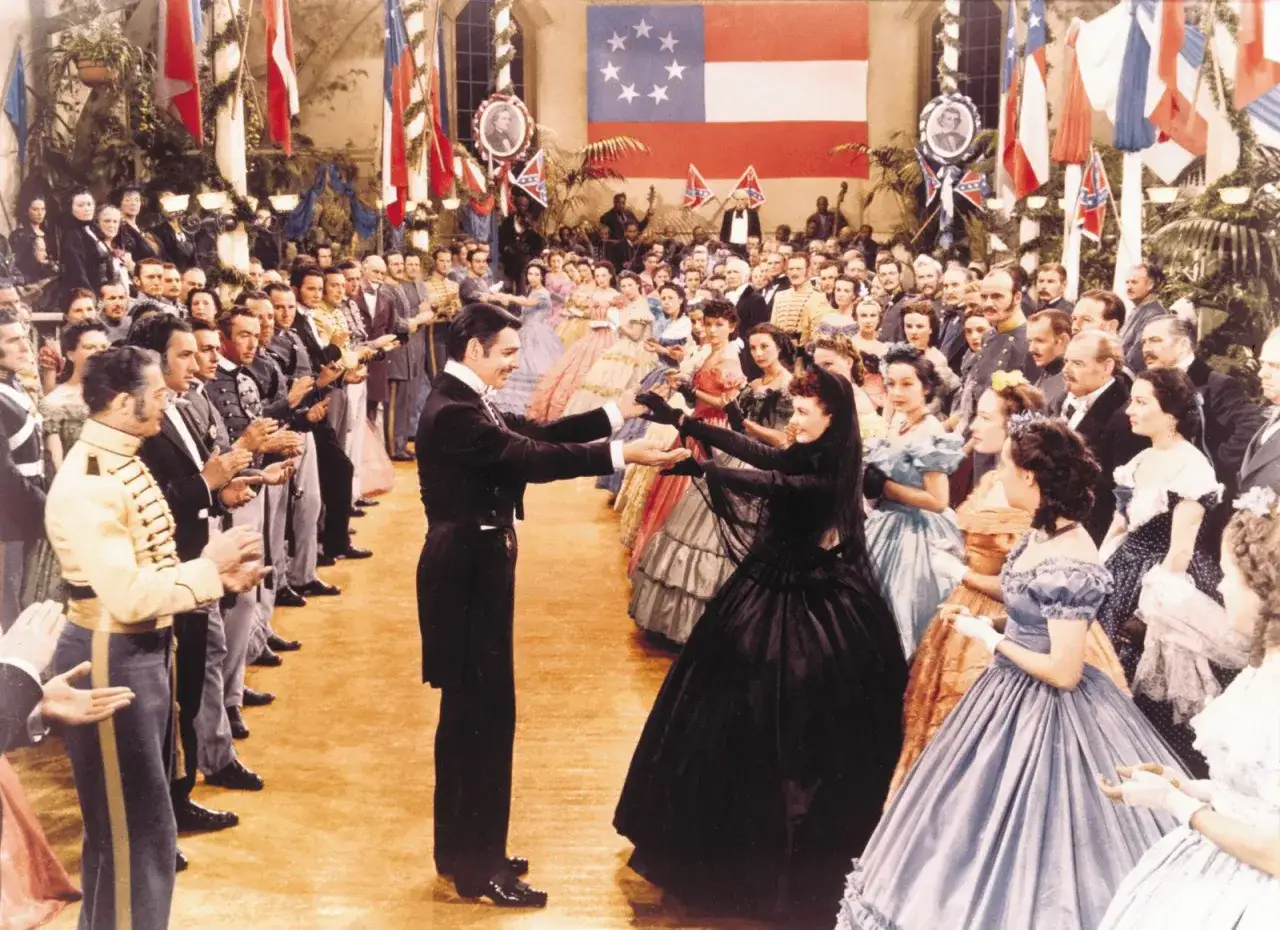 Scarlett O'Hara i Rhett Butler tańczą na balu. W tle widać flagi Konfederacji i tłum gości w strojach z epoki. Obsada 